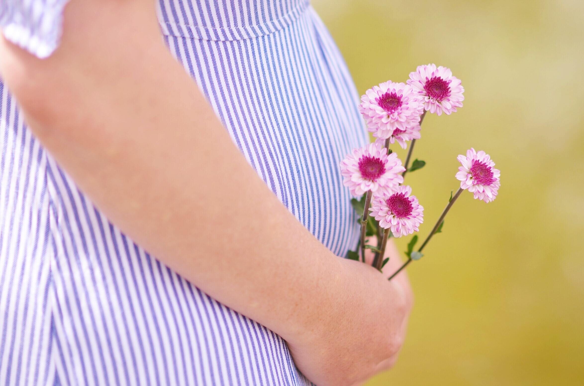 pregnant person holding stomach and holding pink flowers